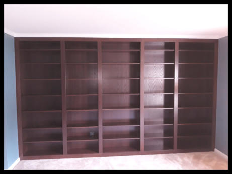 Wall-to-wall Red Oak floor-to-ceiling built-in bookcases with dark rich stain and 3-inch vertical dividers.